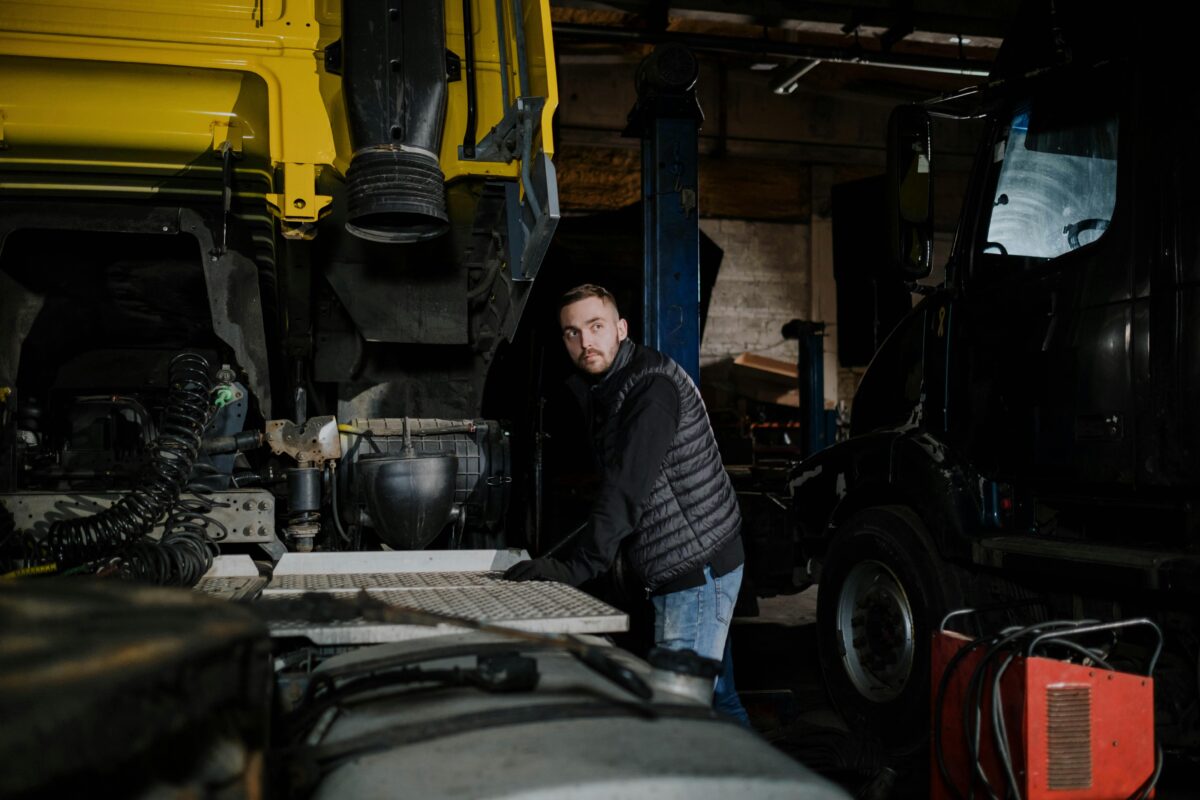 A mechanic in a puffer jacket works on a truck in a dimly lit workshop.